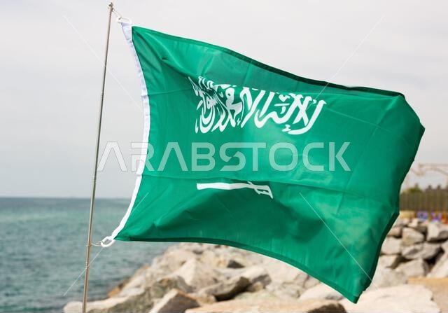 Flag of Saudi Arabia flutters in wind against the backdrop of sea coast