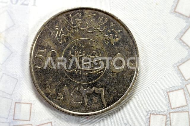 عملة نصف ريال سعودي من فئة 50 هللة، تحمل صورة نخلة مع سيفين متقاطعين واسم الملك عبد الله بن عبد العزيز على الوجه الأمامي، والنقش أ