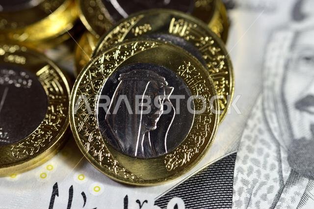 Pile of 1 one Saudi Arabia riyal coin currency features king Salman on 200 SAR two hundred Saudi Arabia riyals banknote bill features king AbdulAziz Pile of 1 one Saudi Arabia riyal coin currency features king Salman on 200 SAR two hundred Saudi Arabia riyals banknote bill features king AbdulAziz