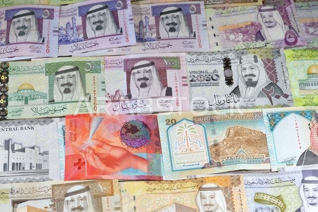 العملات السويسرية من الفرنكات السويسرية والعملات السعودية من الريالات، بقيم مختلفة، تحمل صوراً لملوك المملكة العربية السعودية.