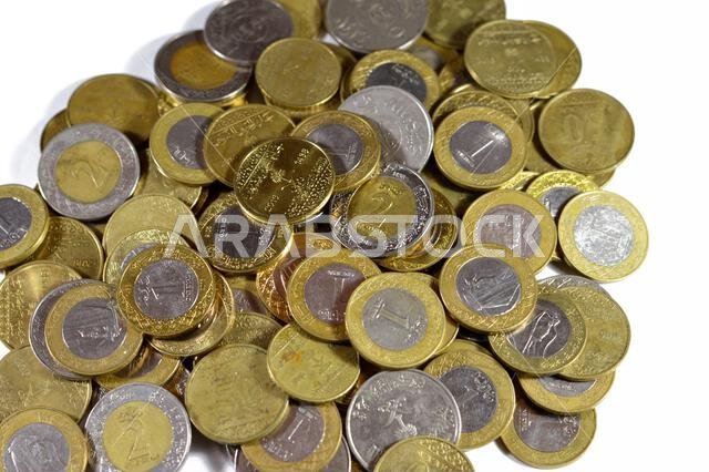 عملات معدنية متنوعة من المملكة العربية السعودية بقيم وأزمنة مختلفة، وعملة الريال السعودي القديمة والجديدة من فئات ريالين، وريال واحد، ونصف ريال، وربع ريال.