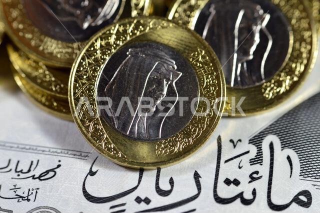 Pile of 1 one Saudi Arabia riyal coin currency features king Salman on  200 SAR two hundred Saudi Arabia riyals banknote bill features king AbdulAziz