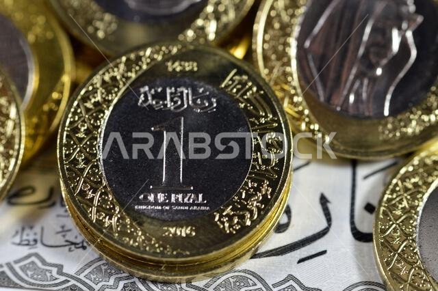 Pile of 1 one Saudi Arabia riyal coin currency features king Salman on 200 SAR two hundred Saudi Arabia riyals banknote bill features king AbdulAziz Pile of 1 one Saudi Arabia riyal coin currency features king Salman on 200 SAR two hundred Saudi Arabia riyals banknote bill features king AbdulAziz