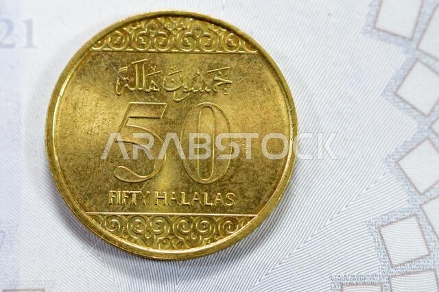 Half riyal golden coin 50 fifty Halalas, features trefoil floral ornamentation on the top and bottom and the arms of Saudi Arabia in the center with t Half riyal golden coin 50 fifty Halalas, features trefoil floral ornamentation on the top and bottom and the arms of Saudi Arabia in the center with t