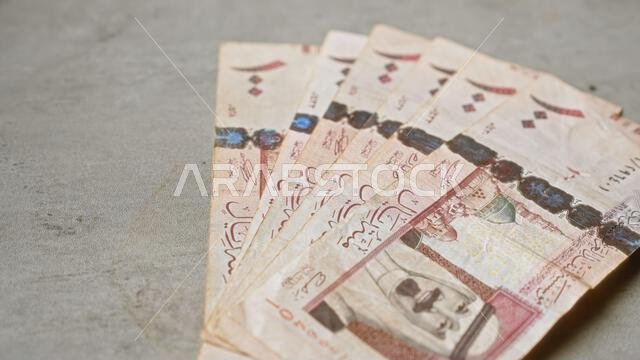 أوراق نقدية سعودية مرتبة على سطح خرساني رمادي اللون، تسلط الضوء على تفاصيل العملة والمواضيع المالية.