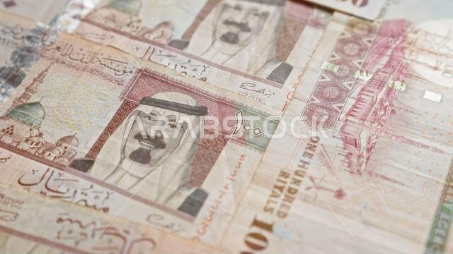 صورة مقرّبة لأوراق نقدية من الريال السعودي، تُظهر تصاميم معقدة وكتابة عربية، تُبرز العملة والتفاصيل الثقافية للمملكة العربية السعودية.