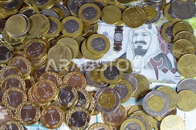 Coins of Saudi Arabian riyal, 2, 1, half and quarter coin on Saudi Arabia money banknotes of riyals bills, of different values, money and economic sta Coins of Saudi Arabian riyal, 2, 1, half and quarter coin on Saudi Arabia money banknotes of riyals bills, of different values, money and economic sta