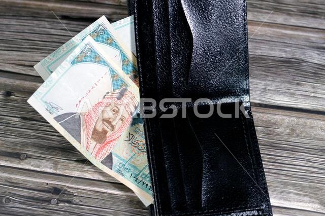 أوراق نقدية من الريال السعودي، رزمة من الأوراق النقدية بالريال السعودي في محفظة جلدية سوداء، شراء، بيع، بيع، المال والوضع الاقتصادي.