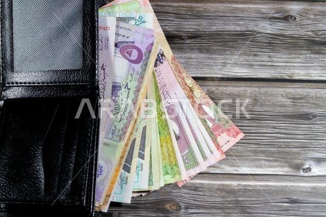 أوراق نقدية من الريال السعودي، رزمة من الأوراق النقدية بالريال السعودي في محفظة جلدية سوداء، شراء، بيع، بيع، المال والوضع الاقتصادي.