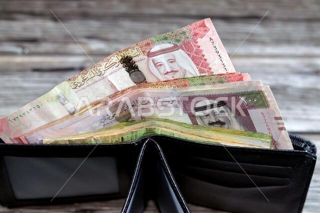 Saudi Arabian Riyals bills banknotes, pile of SAR riyal cash money notes in a black leather wallet, buying, selling, sale, money and economic status,