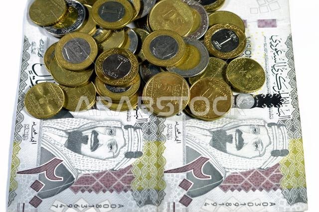 ورقة نقدية من فئة 200 ريال سعودي، تحمل صورة الملك عبد العزيز آل سعود ورؤية المملكة العربية السعودية لعام 2030، بالإضافة إلى عملات معدنية سعودية من فئة ريالين.
