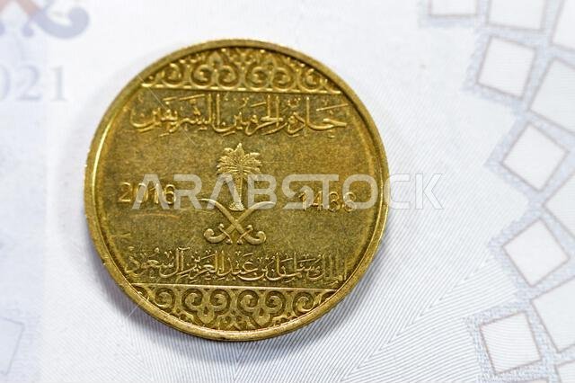 Half riyal golden coin 50 fifty Halalas, features trefoil floral ornamentation on the top and bottom and the arms of Saudi Arabia in the center with t