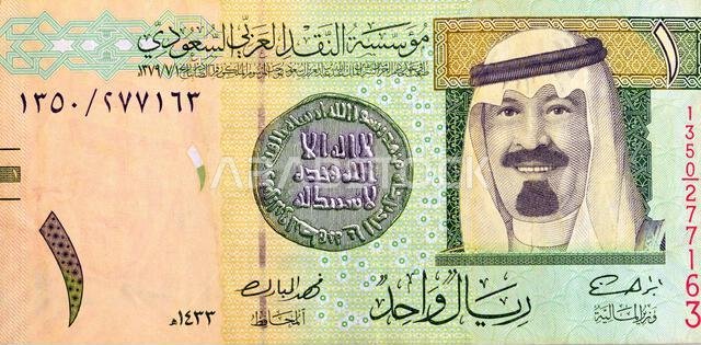 جزء كبير من وجه ورقة نقدية من فئة ريال سعودي واحد (1 ريال سعودي) يحمل صورة الملك عبد الله بن عبد العزيز، وأول عملة إسلامية قديمة.