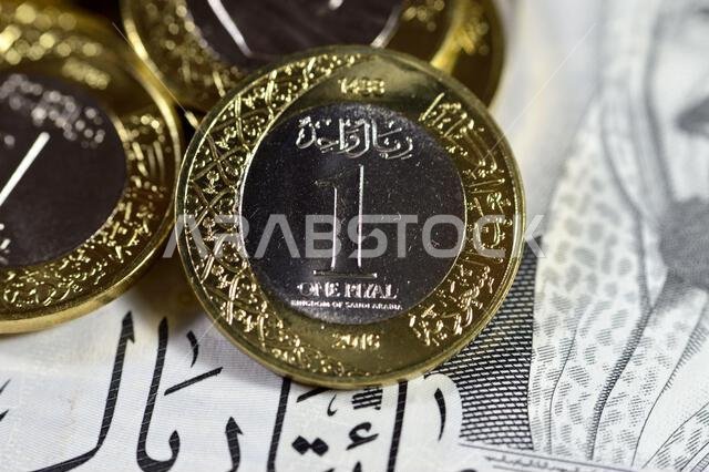 Pile of 1 one Saudi Arabia riyal coin currency features king Salman on  200 SAR two hundred Saudi Arabia riyals banknote bill features king AbdulAziz