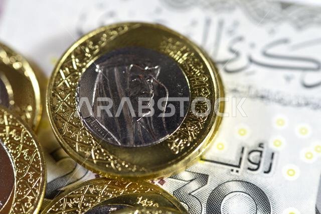 كومة من عملة معدنية من فئة ريال سعودي واحد تحمل صورة الملك سلمان، وفئة 200 ريال سعودي تحمل صورة الملك عبد العزيز.