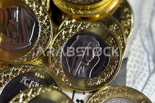 كومة من عملة معدنية من فئة ريال سعودي واحد تحمل صورة الملك سلمان، وفئة 200 ريال سعودي تحمل صورة الملك عبد العزيز.