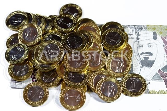 Pile of 1 one Saudi Arabia riyal coin currency features king Salman on  200 SAR two hundred Saudi Arabia riyals banknote bill features king AbdulAziz