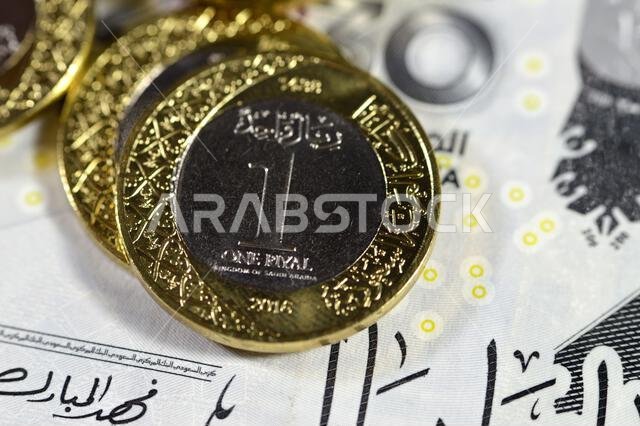 Pile of 1 one Saudi Arabia riyal coin currency features king Salman on  200 SAR two hundred Saudi Arabia riyals banknote bill features king AbdulAziz