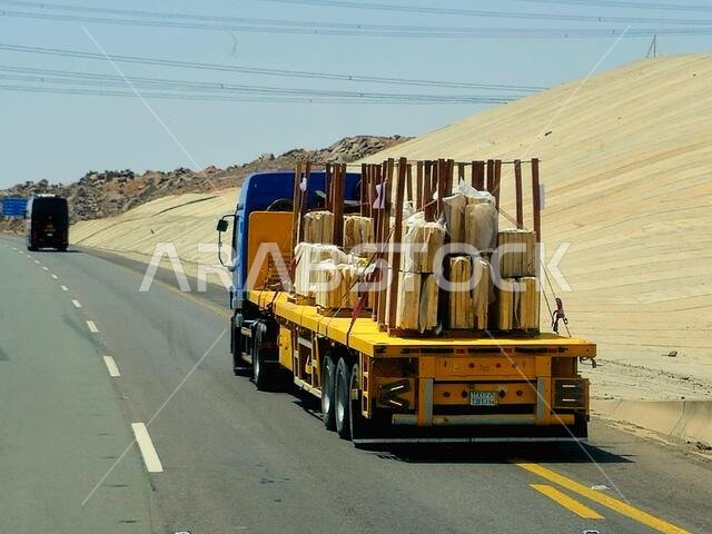 طريق مكة المكرمة - المدينة المنورة، المملكة العربية السعودية، 25 يونيو 2024: شاحنة مسطحة كبيرة محملة بشحنة تُنقل على طريق سريع بواسطة شاحنة نقل كبيرة وبحارة.
