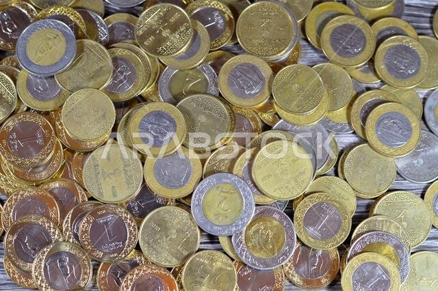 عملات معدنية متنوعة من المملكة العربية السعودية بقيم وأزمنة مختلفة، وعملة الريال السعودي القديمة والجديدة من فئات ريالين، وريال واحد، ونصف ريال، وربع ريال.