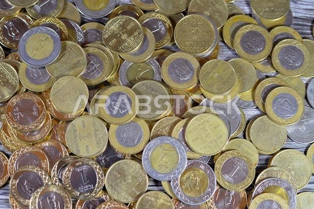 عملات معدنية متنوعة من المملكة العربية السعودية بقيم وأزمنة مختلفة، وعملة الريال السعودي القديمة والجديدة من فئات ريالين، وريال واحد، ونصف ريال، وربع ريال.