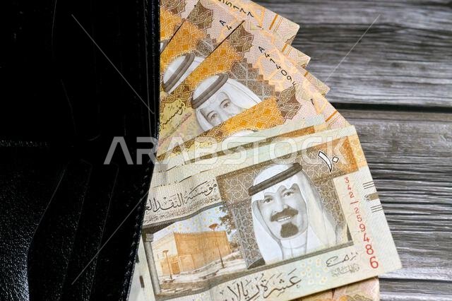 Saudi Arabian Riyals bills banknotes, pile of SAR riyal cash money notes in a black leather wallet, buying, selling, sale, money and economic status,