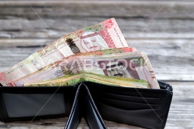 Saudi Arabian Riyals bills banknotes, pile of SAR riyal cash money notes in a black leather wallet, buying, selling, sale, money and economic status,