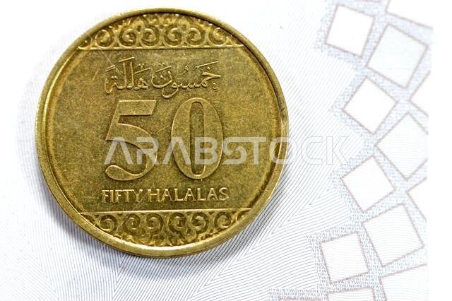 عملة ذهبية نصف ريال (50 هللة)، تتميز بزخارف نباتية ثلاثية الفصوص في الأعلى والأسفل، وشعار المملكة العربية السعودية في المنتصف.