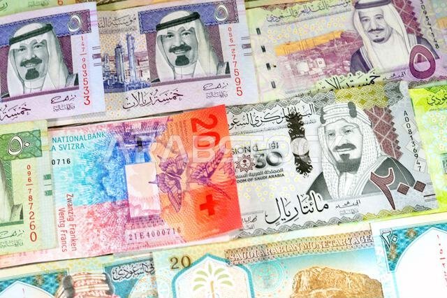 العملات السويسرية من الفرنكات السويسرية والعملات السعودية من الريالات، بقيم مختلفة، تحمل صوراً لملوك المملكة العربية السعودية.