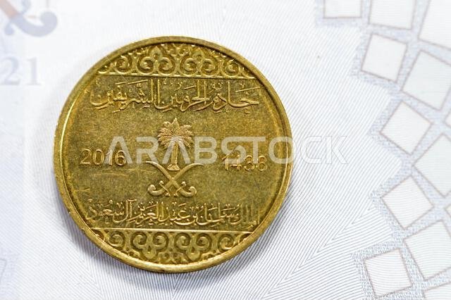 Half riyal golden coin 50 fifty Halalas, features trefoil floral ornamentation on the top and bottom and the arms of Saudi Arabia in the center with t