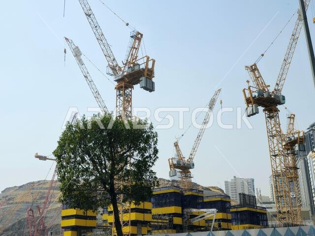 Mecca, Saudi Arabia, June 8 2024: Cranes of a construction site of a new high rise and the mountains of Makkah, Mecca  is the capital of Mecca Provinc