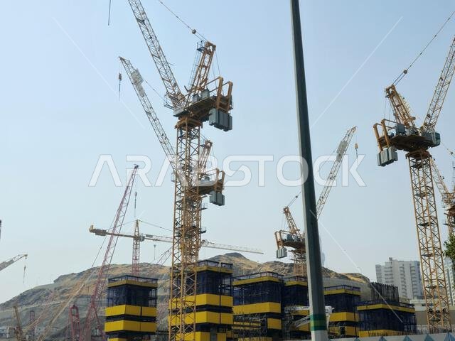 Mecca, Saudi Arabia, June 8 2024: Cranes of a construction site of a new high rise and the mountains of Makkah, Mecca  is the capital of Mecca Provinc