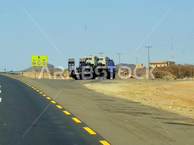 طريق مكة المكرمة - المدينة المنورة، المملكة العربية السعودية، 25 يونيو 2024: شاحنة مسطحة كبيرة محملة بشحنة تُنقل على طريق سريع بواسطة شاحنة نقل كبيرة وبحارة.