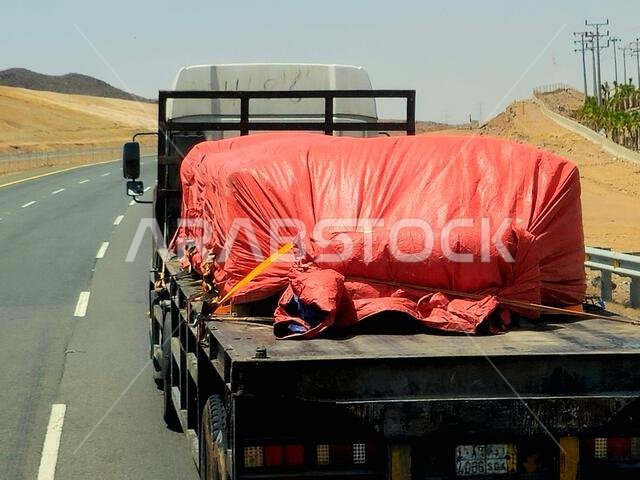 طريق مكة المكرمة - المدينة المنورة، المملكة العربية السعودية، 25 يونيو 2024: شاحنة مسطحة كبيرة محملة بشحنة تُنقل على طريق سريع بواسطة شاحنة نقل كبيرة وبحارة.