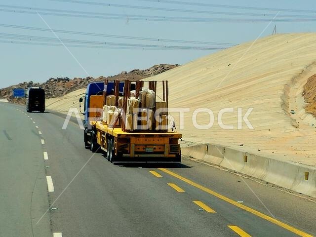 طريق مكة المكرمة - المدينة المنورة، المملكة العربية السعودية، 25 يونيو 2024: شاحنة مسطحة كبيرة محملة بشحنة تُنقل على طريق سريع بواسطة شاحنة نقل كبيرة وبحارة.