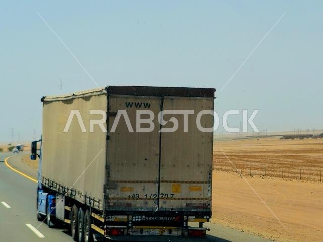 طريق مكة المكرمة - المدينة المنورة، المملكة العربية السعودية، 25 يونيو 2024: شاحنة مسطحة كبيرة تحمل حاوية شحن فولاذية على طريق سريع في السعودية، شحن و