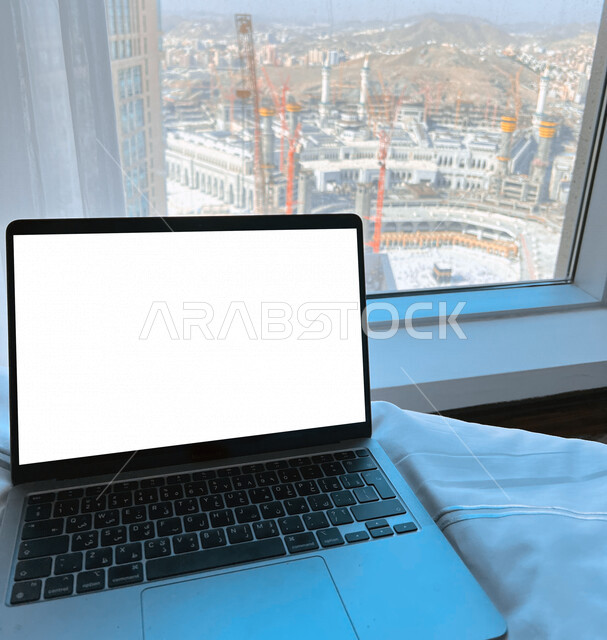 An image of a laptop computer with a blank white screen with a background of the Holy Mosque in Makkah Al-Mukarramah, advertising and promotion, marketing for programs and applications, using modern technologies