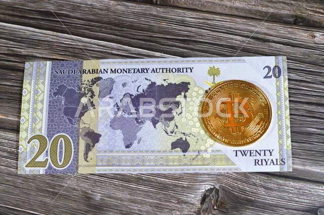 عملة الريال السعودي الورقية مزودة بعملة بيتكوين ذهبية مادية، بيتكوين هي أول عملة مشفرة لامركزية، وعقد في شبكة بيتكوين من نظير إلى نظير للتحقق من المعاملات