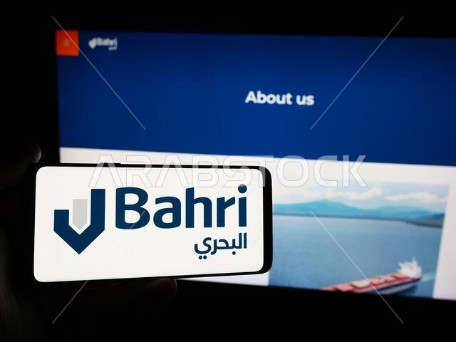في هذه الصورة التوضيحية، يظهر شخص يحمل هاتفًا محمولًا عليه شعار شركة النقل البحري الوطنية السعودية (بحري) أمام صفحة ويب.