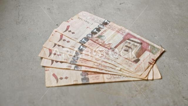 انتشرت أوراق نقدية من الريال السعودي على سطح خرساني خشن، مما أبرز تفاصيل العملة والتصاميم التقليدية في عرض مقرب.