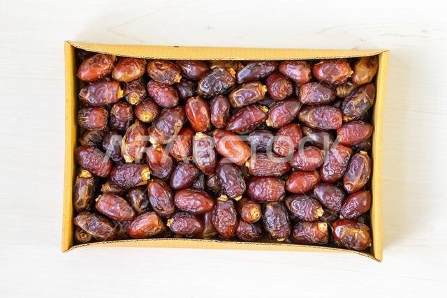 Top view of fresh dried date palm fruits in a cardboard box on a light wooden surface. This fruit is widely enjoyed during the Islamic holy month of R