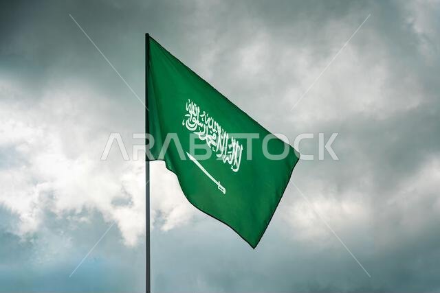 العلم السعودي يرفرف في سماء ملبدة بالغيوم. يرفرف في السماء. العلم السعودي على خلفية سماء ملبدة بالغيوم