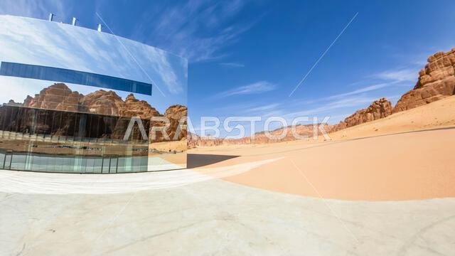 الحِجر، العلا، المملكة العربية السعودية - 5 يناير 2025: واجهة الجدار العاكس العملاق لقاعة مرايا للحفلات الموسيقية، يعكس السماء الزرقاء والمناظر الطبيعية الصحراوية الصخرية.