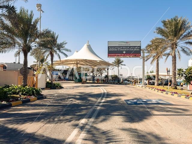 المنامة، البحرين - 5 يناير 2025: معبر جسر الملك فهد الحدودي، الذي يُبرز البنية التحتية الحديثة والطرق المزدانة بأشجار النخيل تحت ضوء أزرق صافٍ