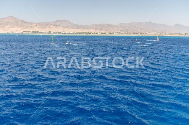 Expansive view of Red Sea with vibrant blue waves under cloudless sky. Distant mountains line horizon, creating striking contrast. Tranquil seascape e