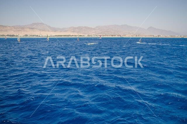 Expansive view of Red Sea with vibrant blue waves under cloudless sky. Distant mountains line horizon, creating striking contrast. Tranquil seascape e