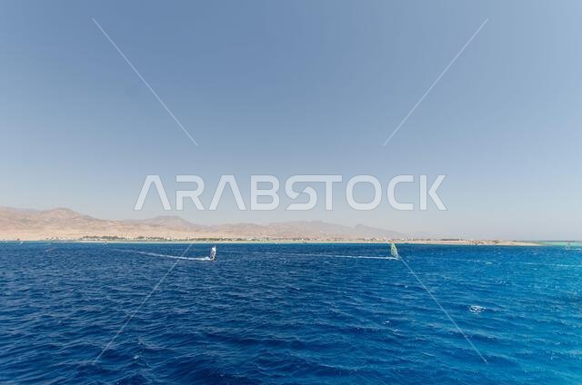 Expansive view of Red Sea with vibrant blue waves under cloudless sky. Distant mountains line horizon, creating striking contrast. Tranquil seascape e