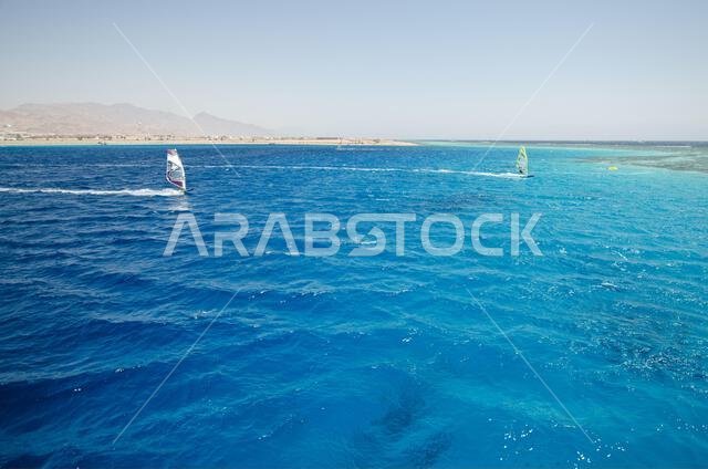 Expansive view of Red Sea with vibrant blue waves under cloudless sky. Distant mountains line horizon, creating striking contrast. Tranquil seascape e