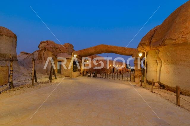 شارع مضاء وقوس يؤدي إلى مبانٍ تقليدية في كهوف جبل القرح الصخرية ليلاً في واحة الأحساء، المملكة العربية السعودية شارع مضاء وقوس يؤدي إلى مبانٍ تقليدية في كهوف جبل القرح الصخرية ليلاً في واحة الأحساء، المملكة العربية السعودية