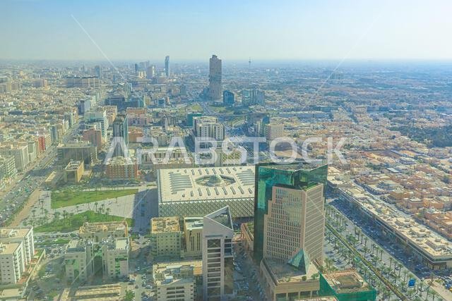منظر بانورامي لمدينة الرياض، المملكة العربية السعودية، يُظهر امتدادها الحضري الشاسع، وشوارعها الصاخبة، وهندستها المعمارية الحديثة تحت سماء مشرقة مشمسة.